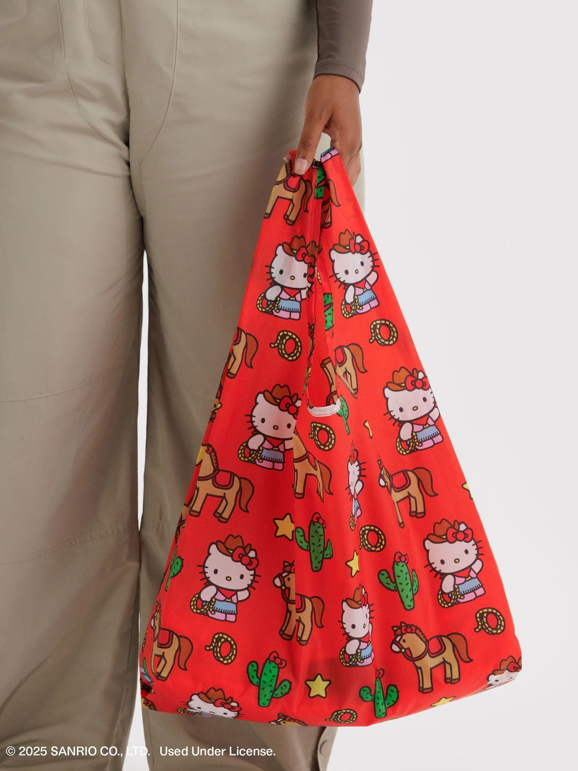 Red bag with Hello Kitty and horse pattern held by a person wearing beige pants.