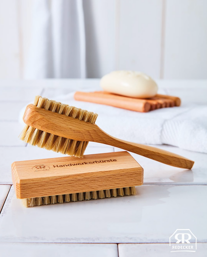 Wooden brush with bristles on a wooden block, placed on a white surface with a blurred background.