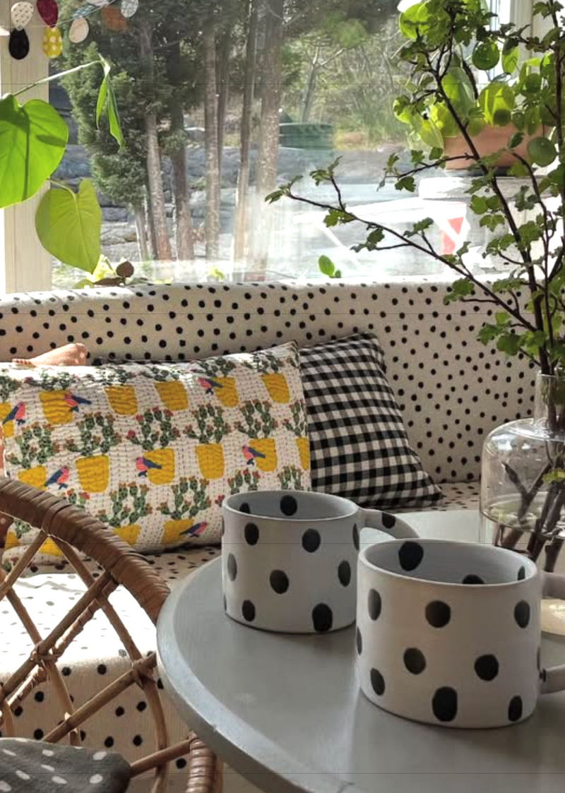 Polka dot cushions on a sofa with polka dot planters on a table, surrounded by greenery.