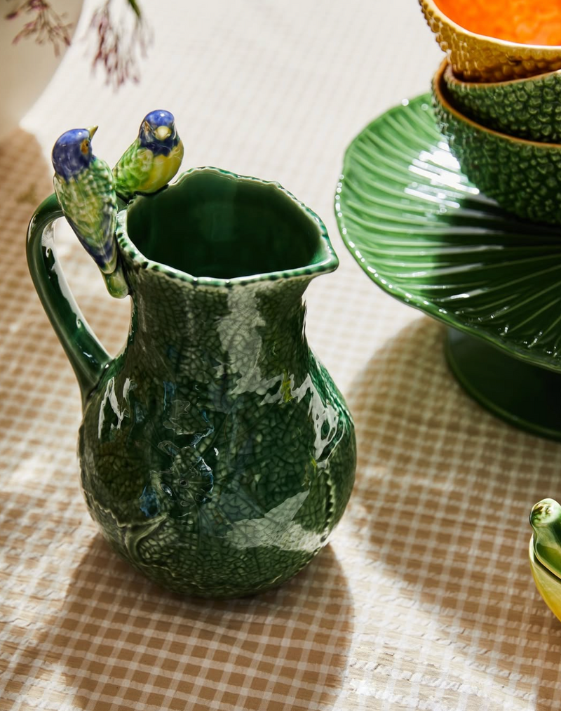Green ceramic pitcher with two ceramic  bird figurines sitting on the edge