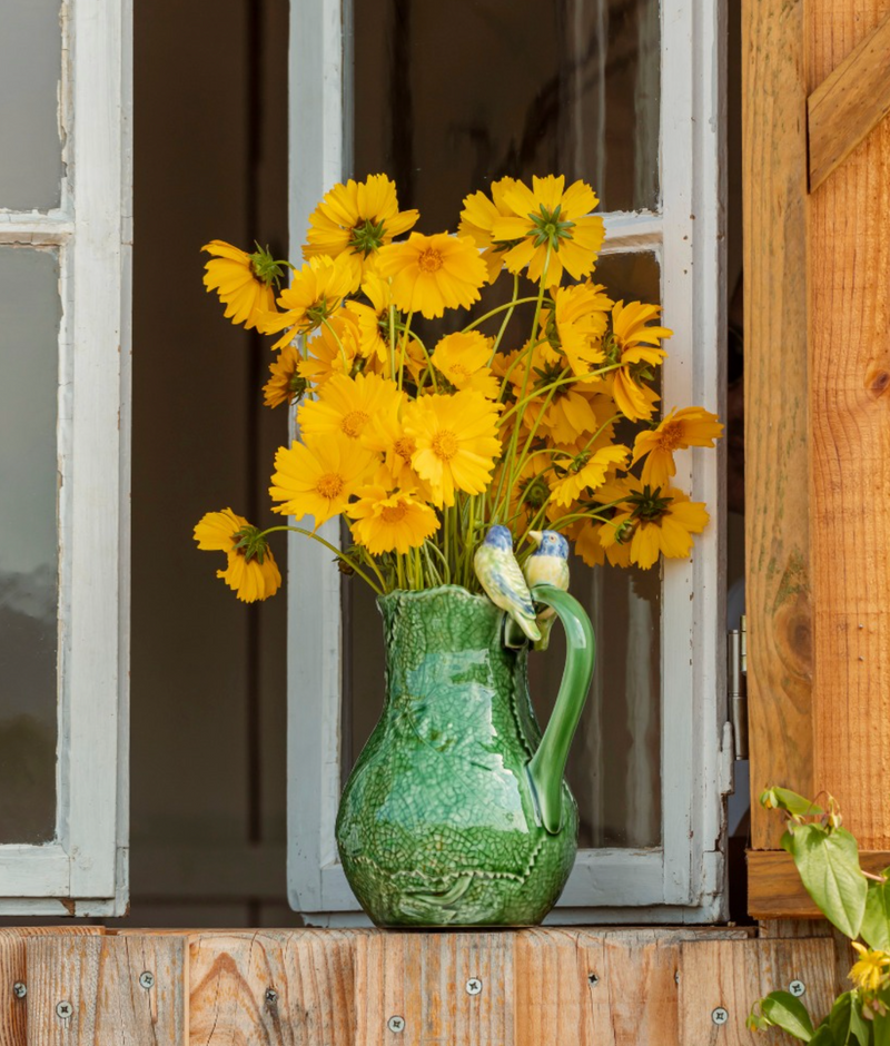 Green pitcher with yellow flowers against a wooden background