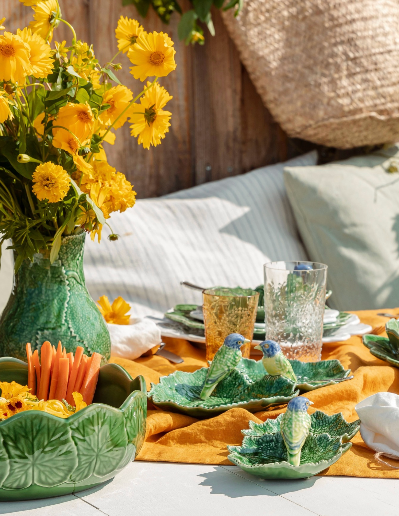 Outdoor setting with a table set for a meal, featuring yellow flowers and green ceramic plates.