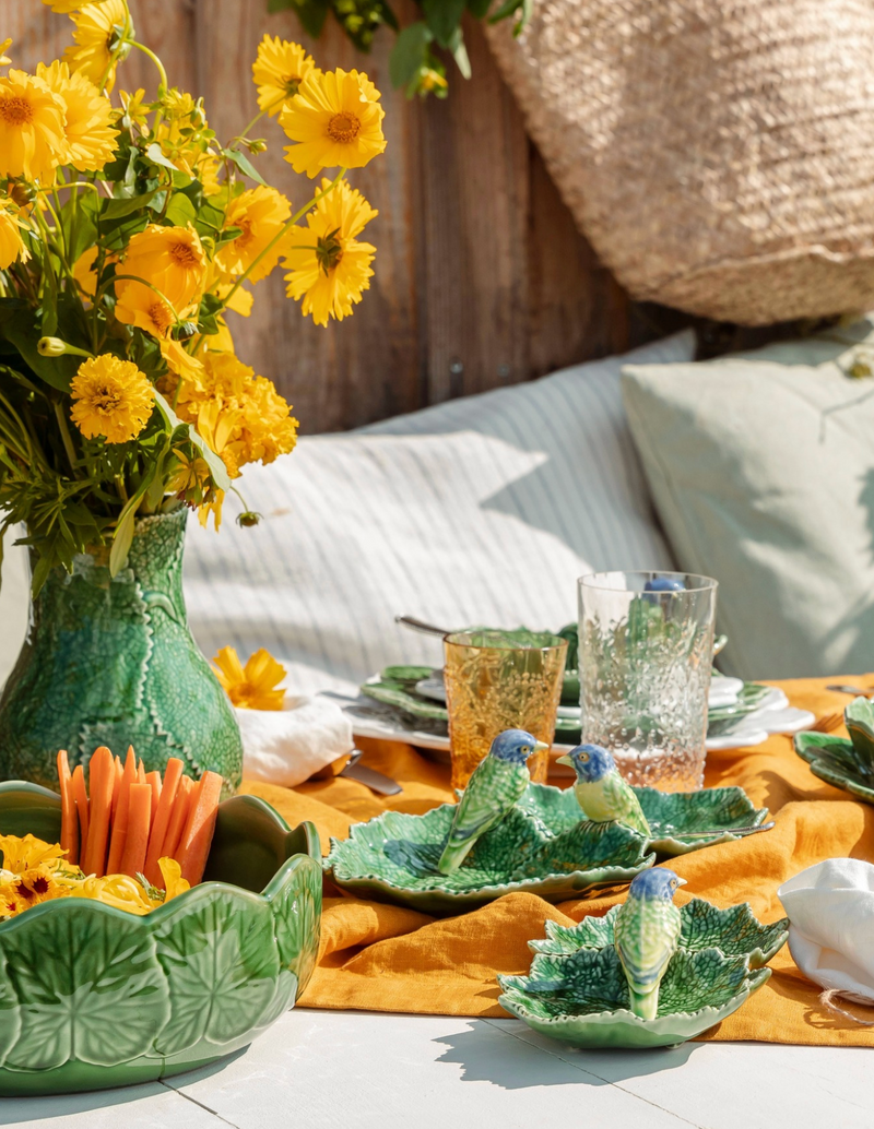 Outdoor setting with a table set for a meal, featuring yellow flowers and green ceramic plates.