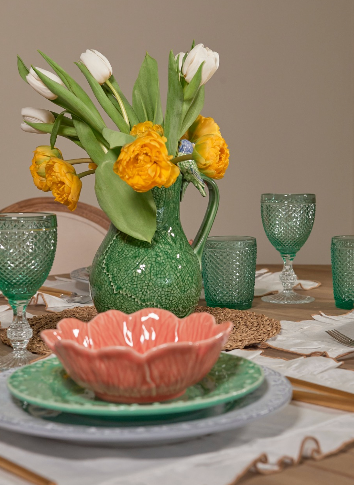 Decorative table setting with a green vase holding flowers, pink bowl, and green glasses.