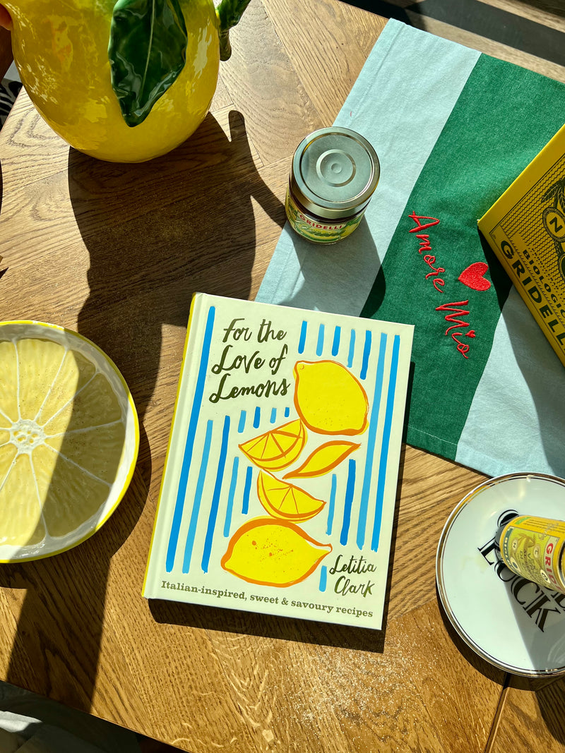 Book titled 'For the Love of Lemons' on a wooden table with lemons and a napkin.