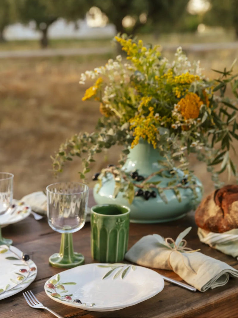Table setting with floral arrangement, green teapot, and decorative plates outdoors.