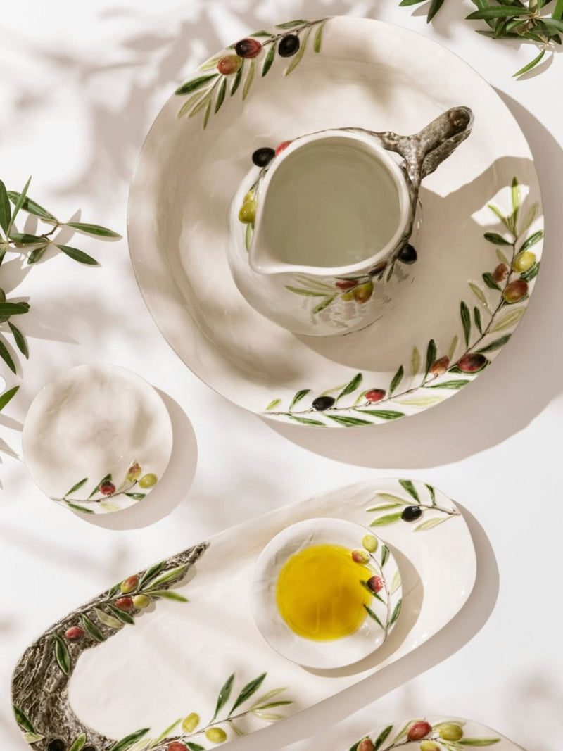 Dining table setting with ceramic plates and pitcher featuring olive design.