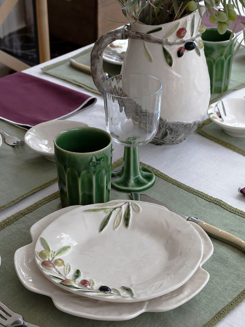 Dining table setting with ceramic plates, cups, and a vase on a green tablecloth.