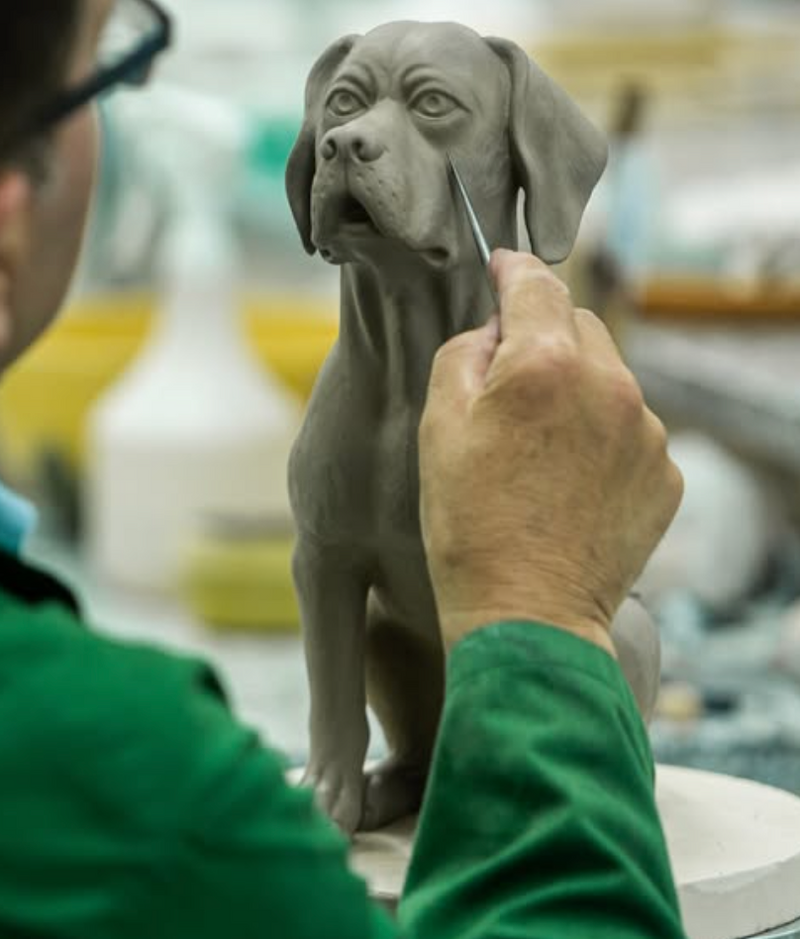 Person working on a dog pitcher with a tool in a workshop setting of Bordallo Pinheiro in Portugal