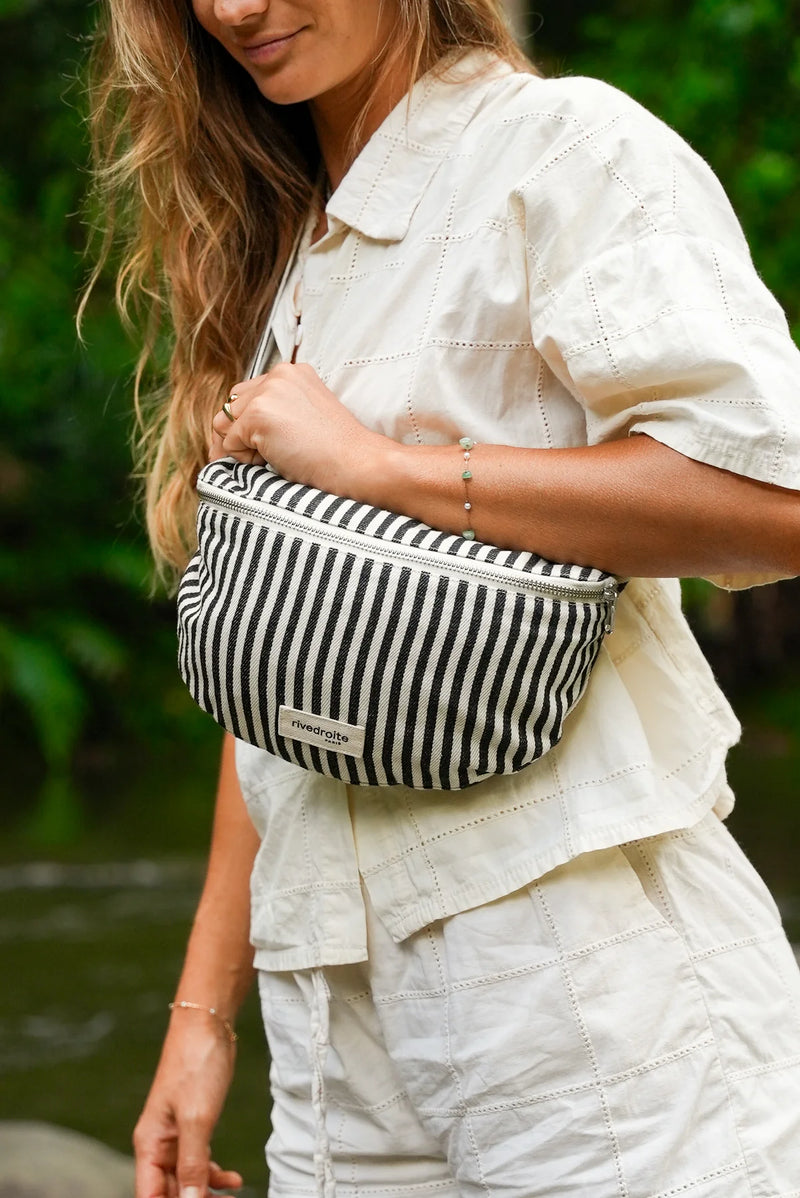 Person wearing a black and white striped fanny pack with a blurred natural background