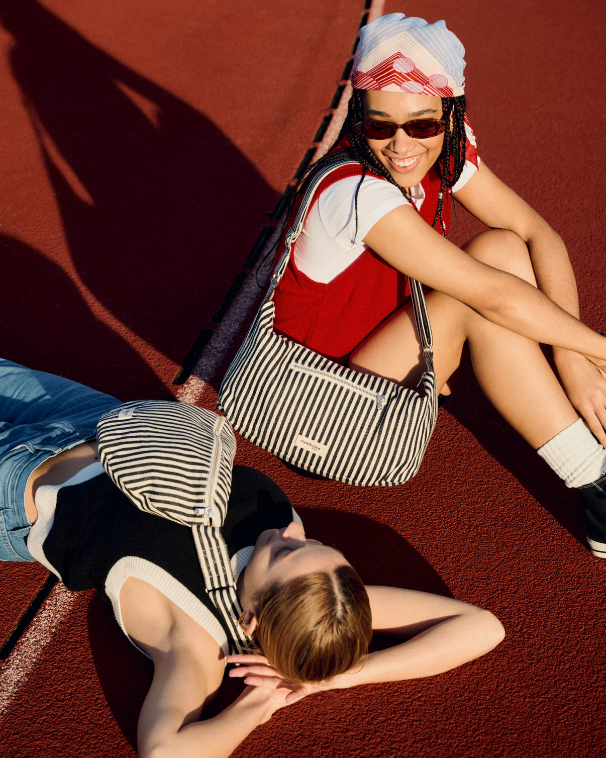 Two people sitting on a red surface, one holding a striped bag.