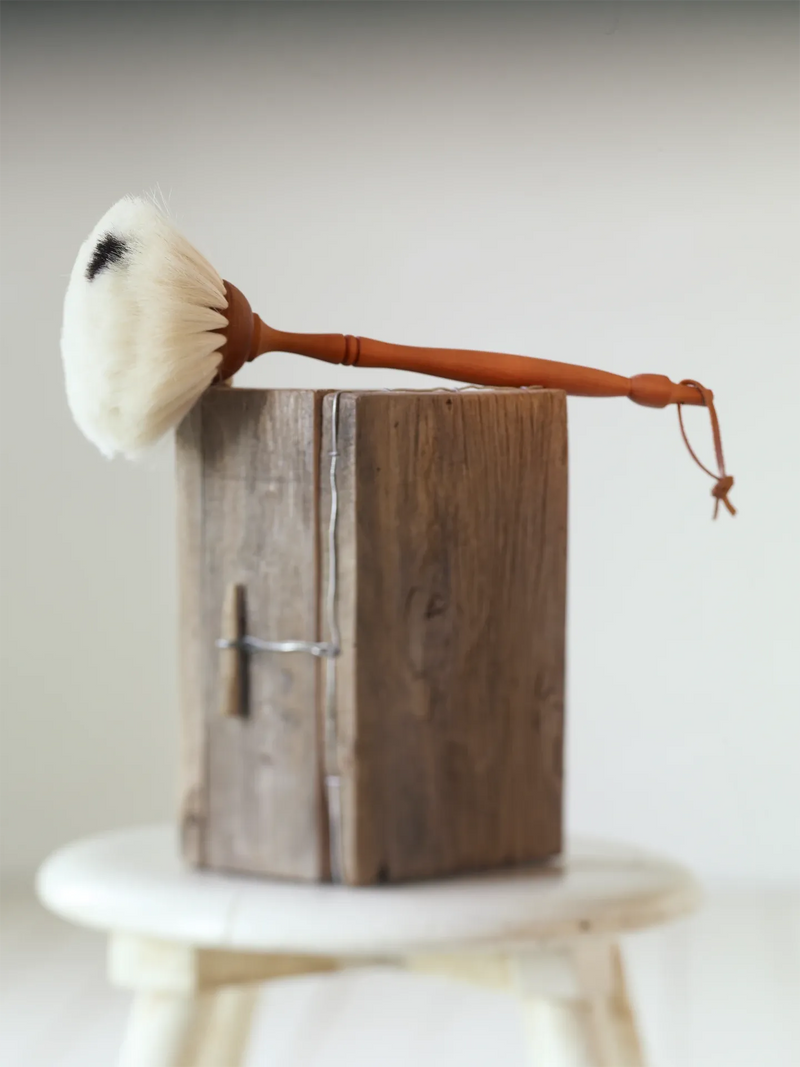 Brush with a wooden handle on a wooden block against a plain background