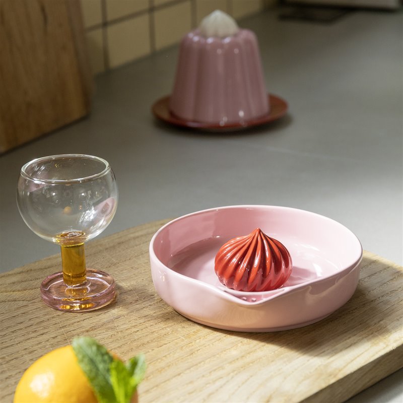 Pink dish with a red dumpling on a wooden surface, with a glass of beer and a lemon in the foreground.