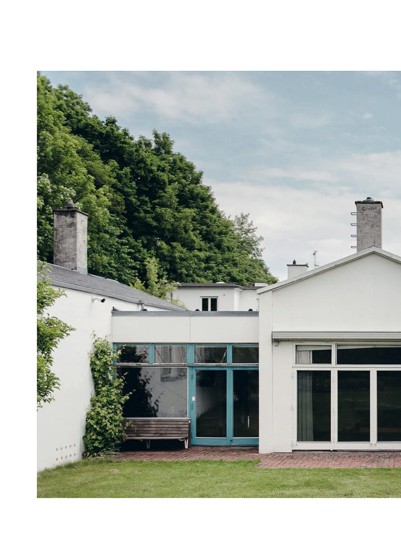 White modernistic atelier house photographed against leafy green forest and blue sky