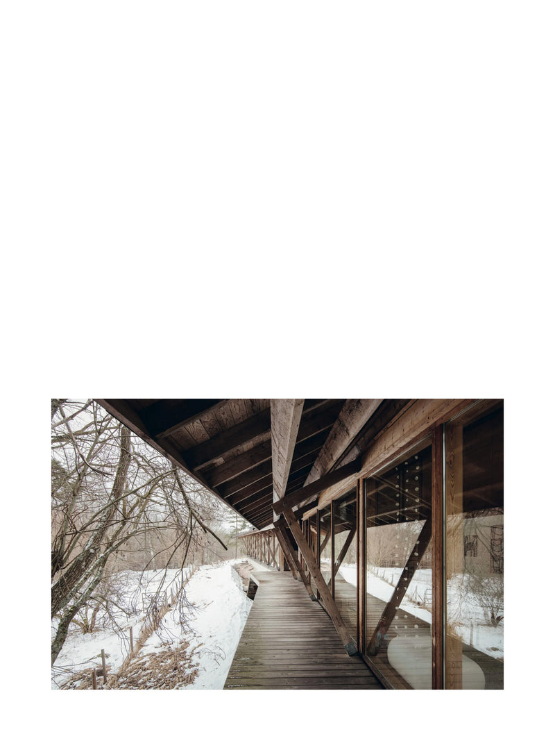 Wooden walkway leading into a building with snow-covered ground and trees in the background