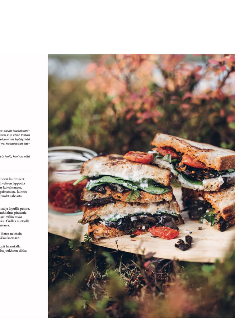 Page of the book has a photo of stack of ricotta and forest mushroom sandwiches on a wooden board with a blurred berry bushes on the  background