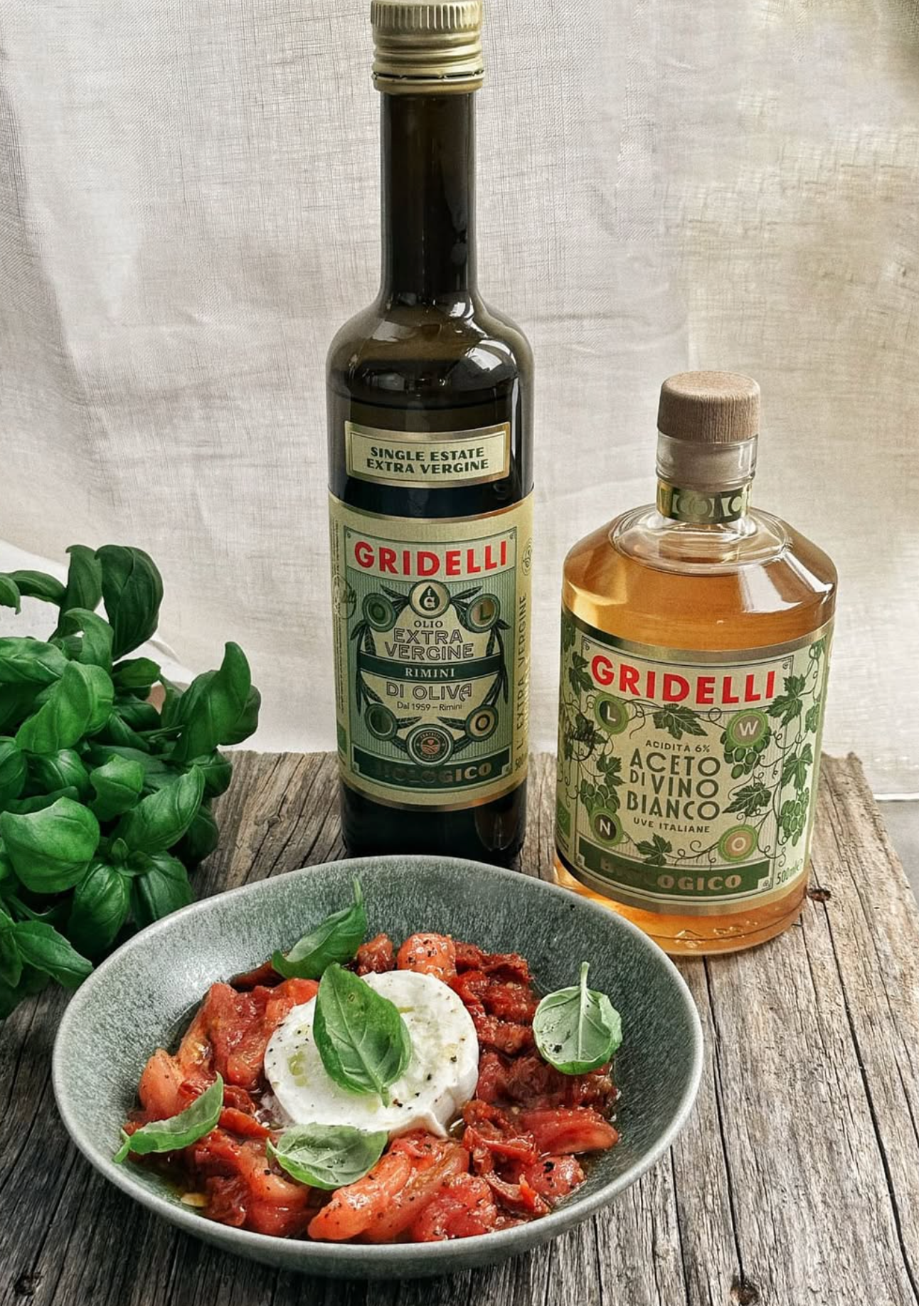 Two bottles of Gridelli olive oil and white wine on a wooden surface with a dish of food.