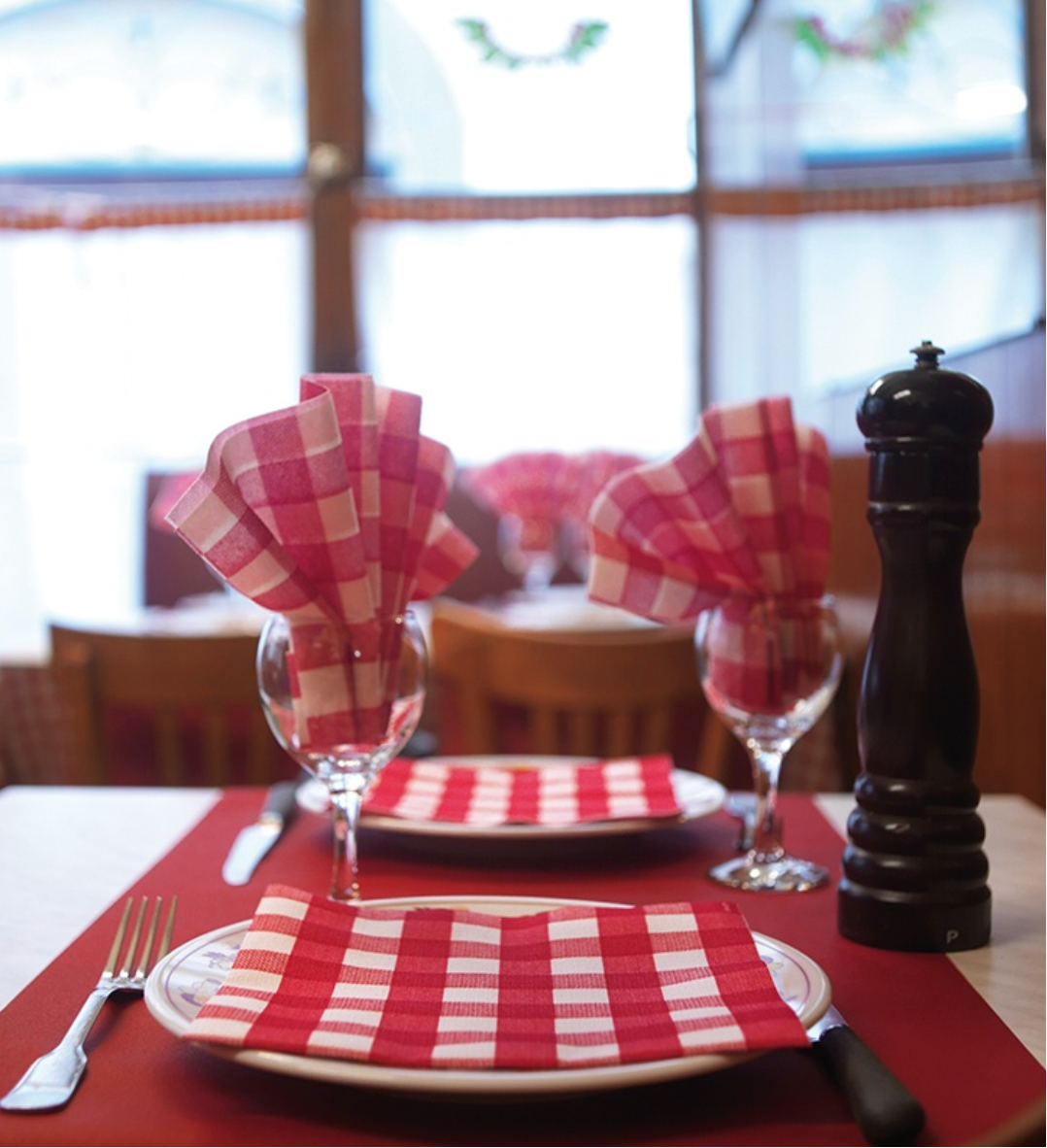 Dining table setting with red and white checkered tablecloth, napkins, and cutlery.