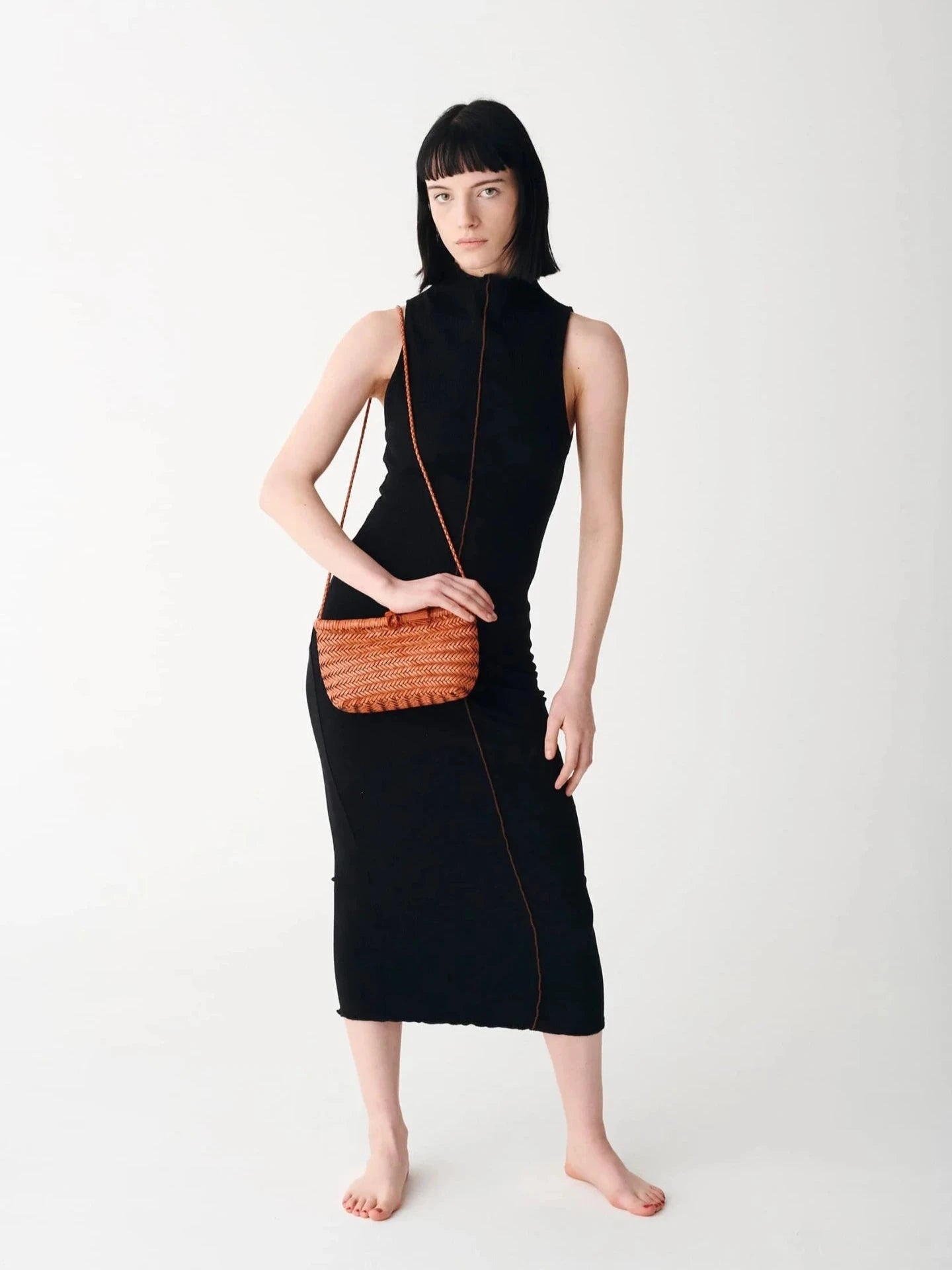 Woman wearing a black sleeveless dress holding an orange handbag on a white background