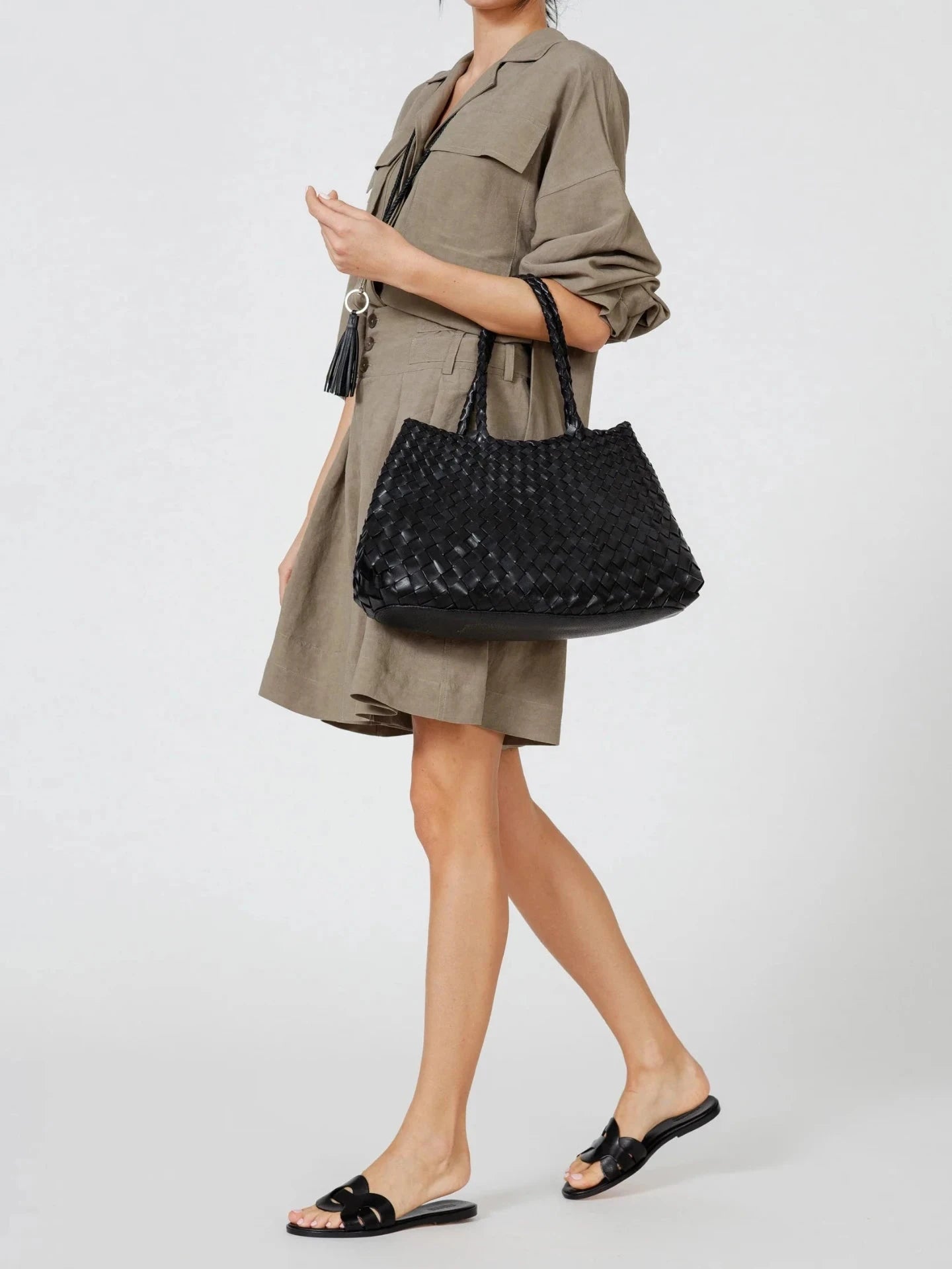 Person wearing a green dress and black sandals, holding a black textured handbag on a white background