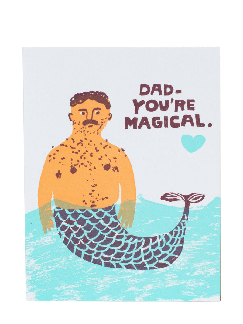 A square greeting card featuring a humorous illustration of a man with a mustache and beard, transformed into a mermaid with a blue and purple scale-patterned tail. The text reads 'DAD - YOU'RE MAGICAL.
