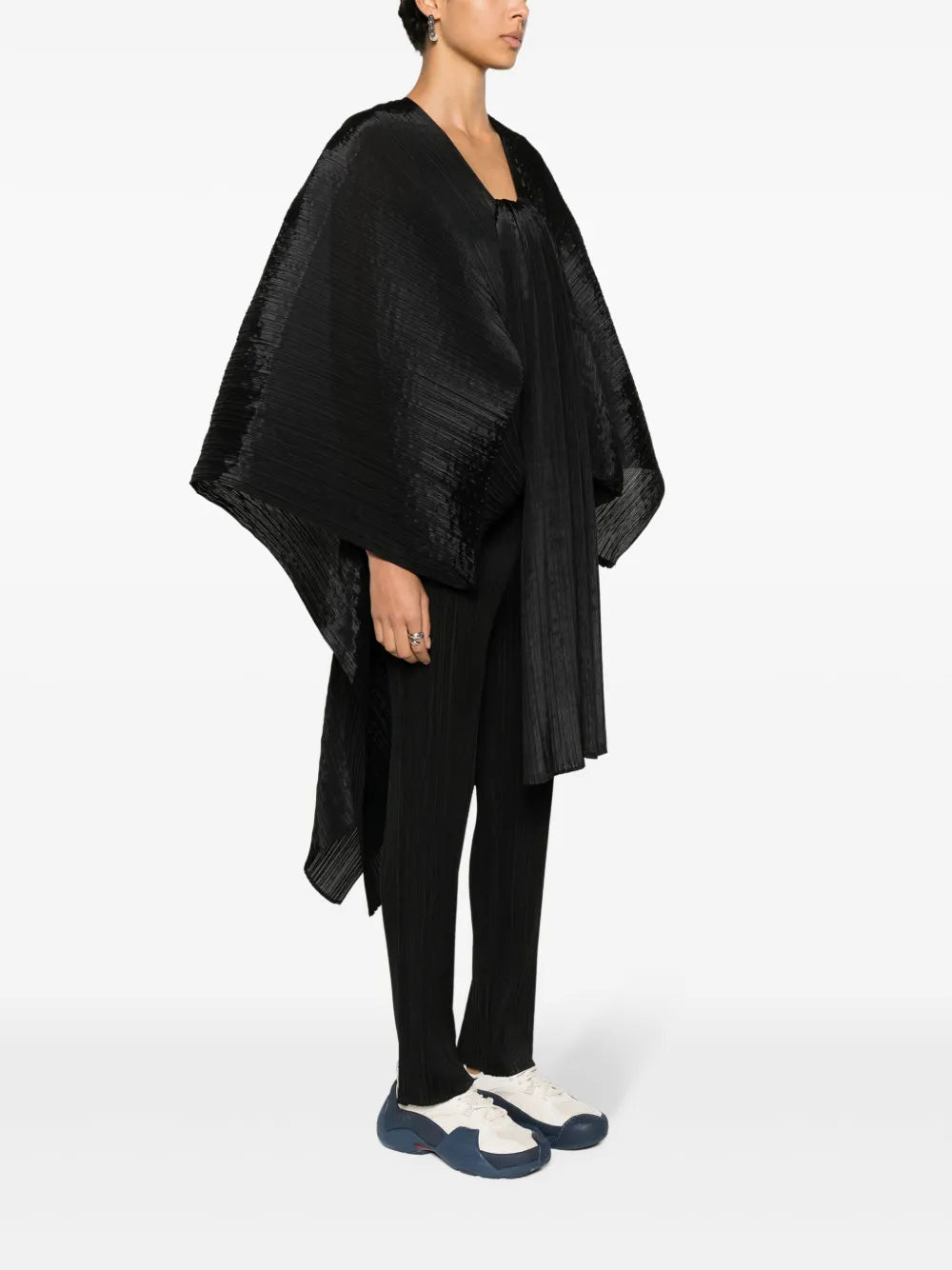 Person wearing a black poncho over a black outfit on a white background