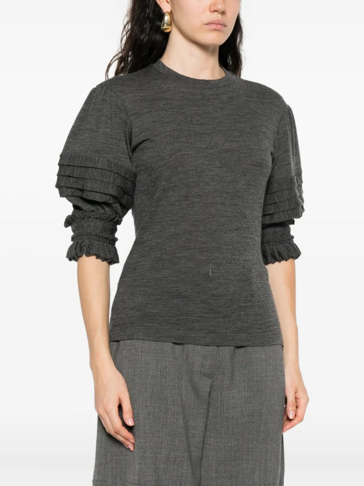 Person wearing a dark gray ruffled sleeve top on a white background