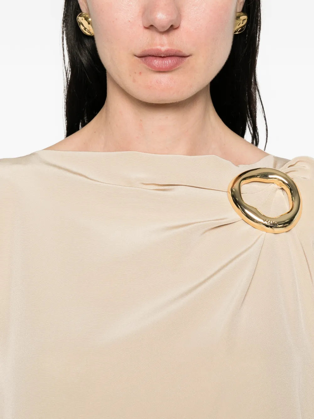 Close-up of a beige dress with a large gold brooch on a white background