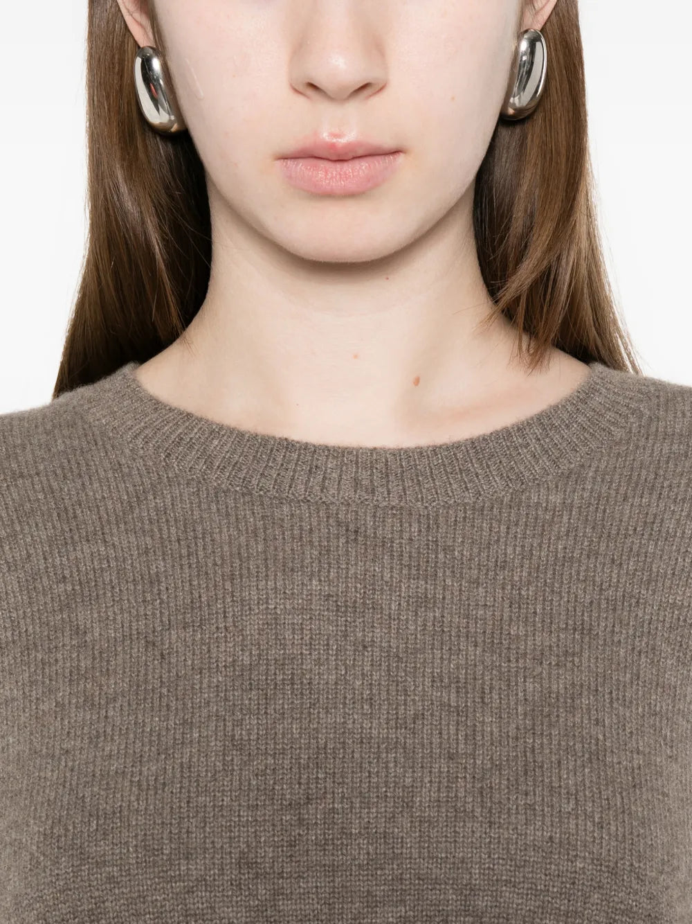 Close-up of a person wearing a brown sweater with earrings on a white background