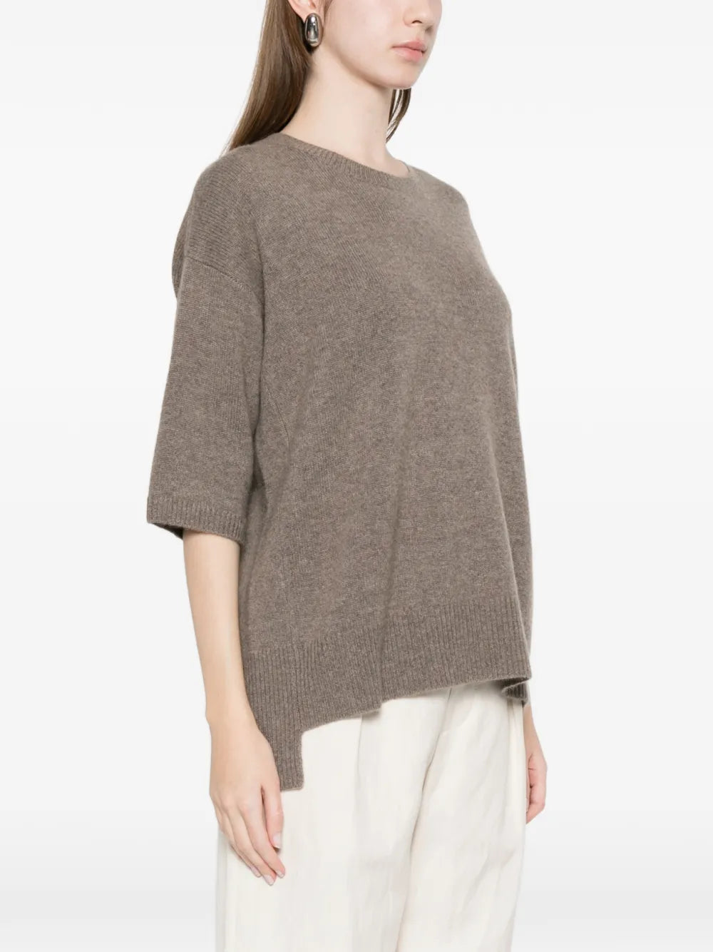 Person wearing a brown sweater and white pants on a white background