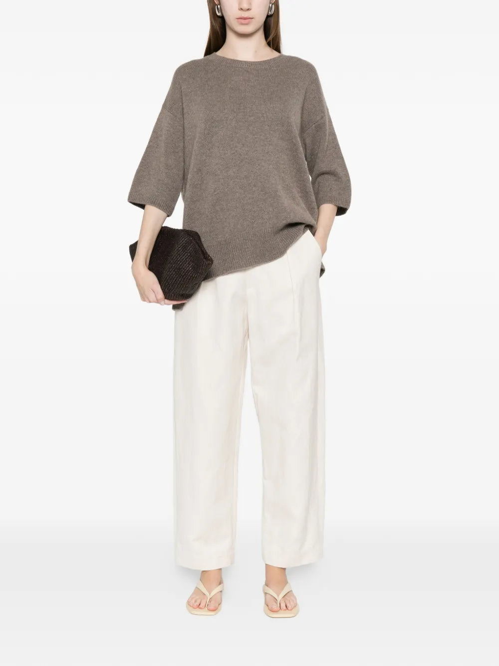 Person wearing a brown sweater and white pants on a white background