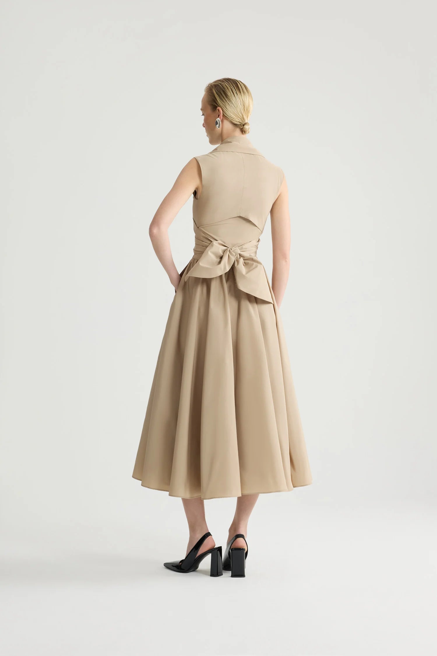 Woman wearing a beige sleeveless dress with a bow detail on a white background