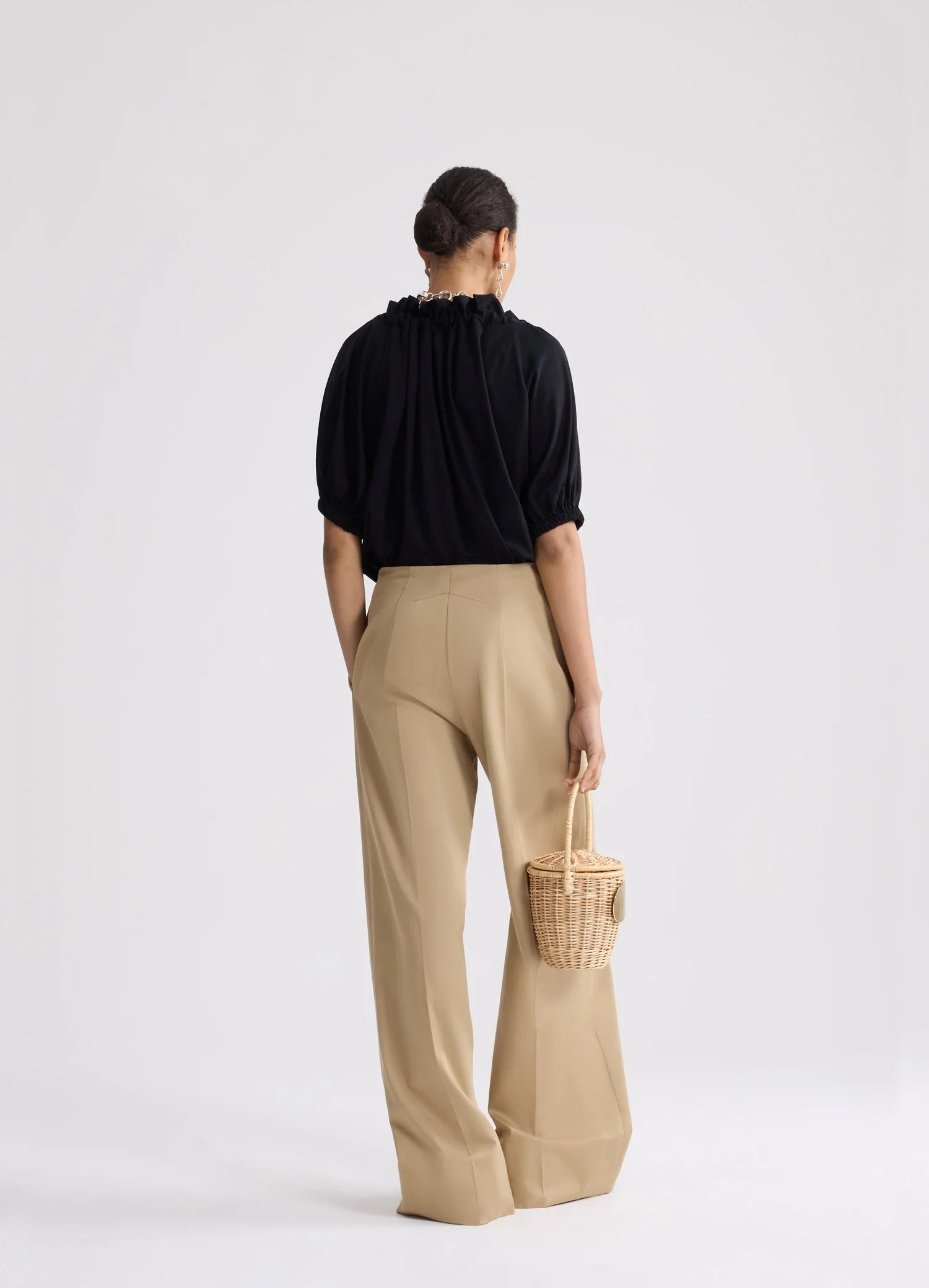 Person wearing a black top and beige pants holding a woven basket on a white background