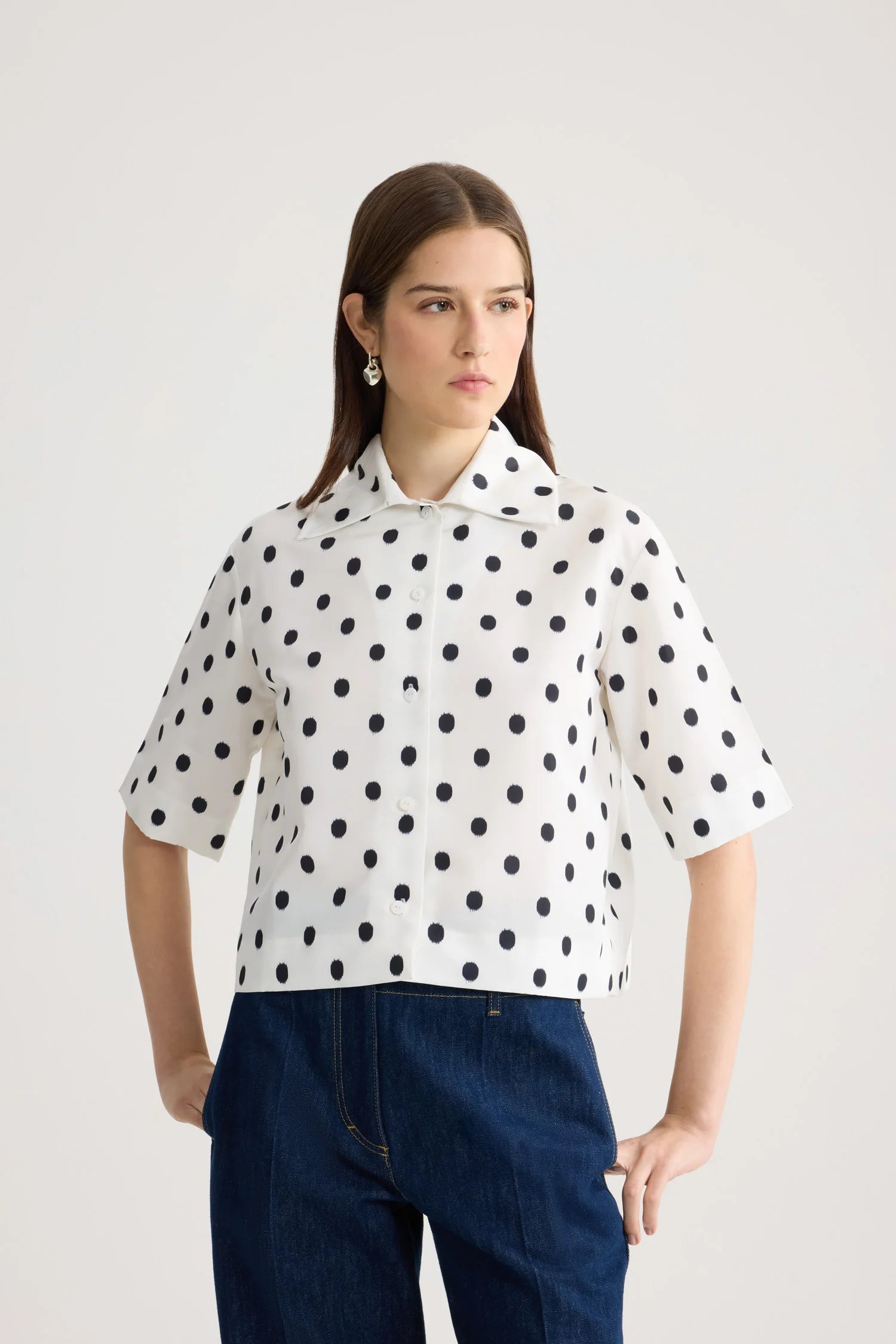 Woman wearing a white blouse with black polka dots and blue pants on a light background