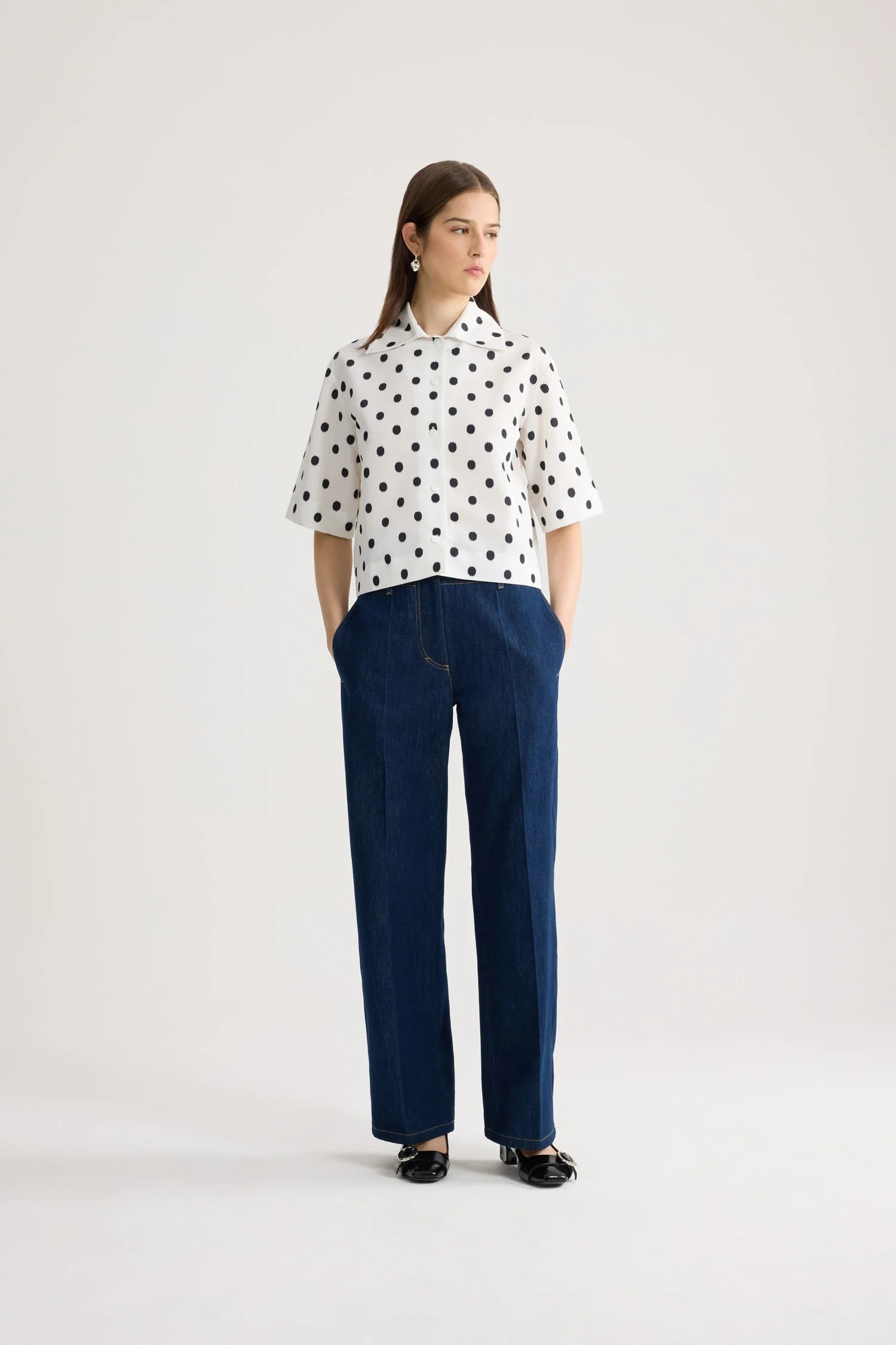 Woman wearing a white blouse with black polka dots and blue pants on a white background