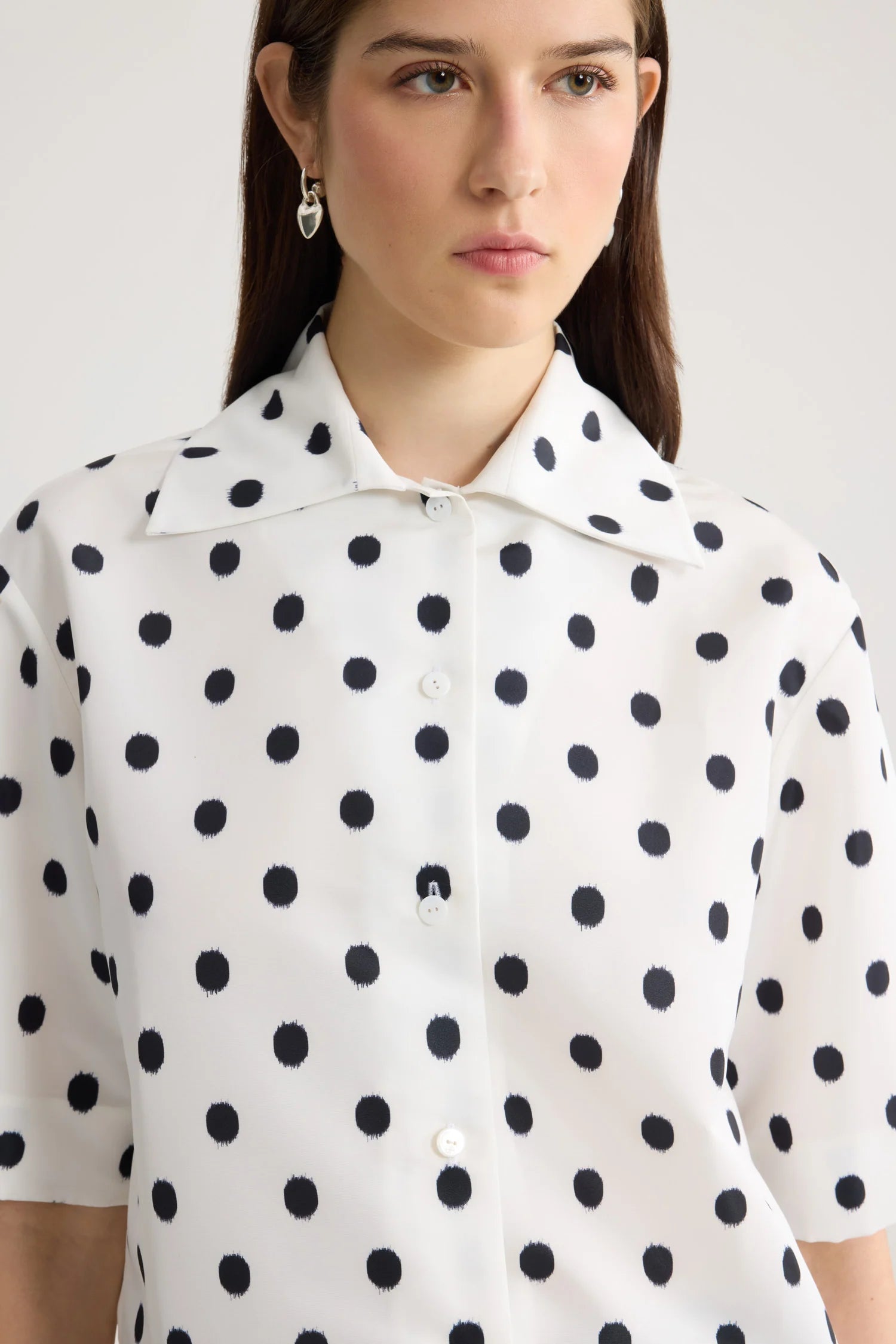 Woman wearing a white blouse with black polka dots against a plain background