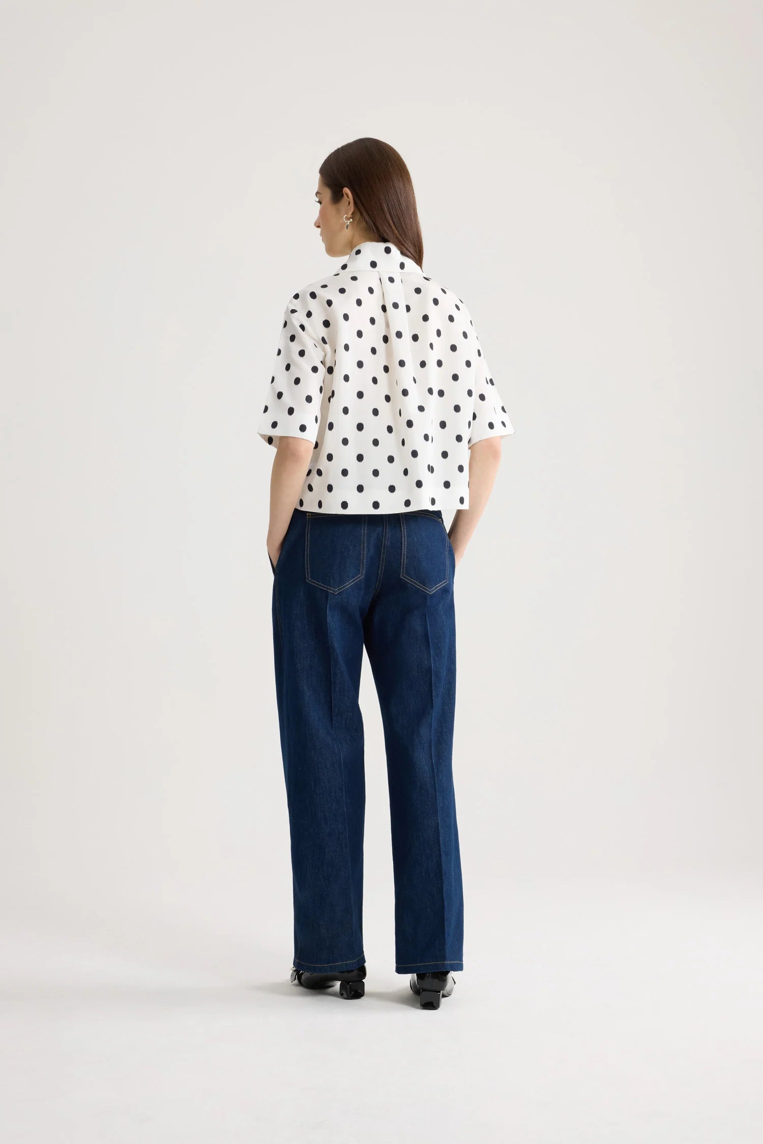Person wearing a white shirt with black polka dots and blue jeans on a white background