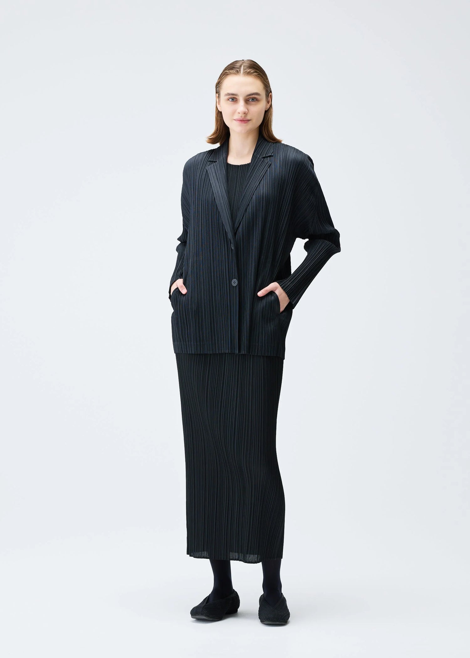 Woman wearing a black pleated blazer & skirt on a white background