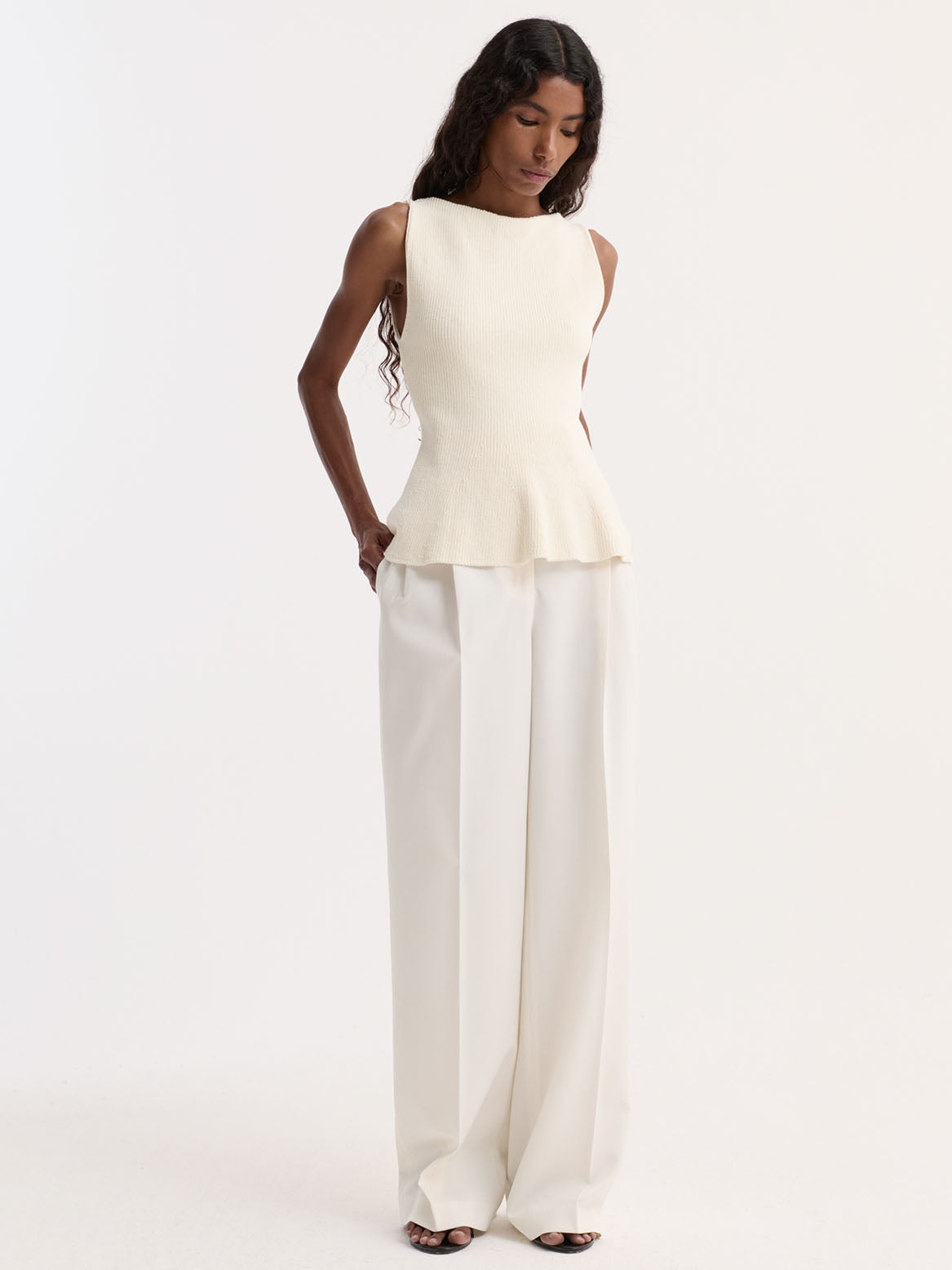 Woman wearing a white peplum top and wide-leg pants on a white background