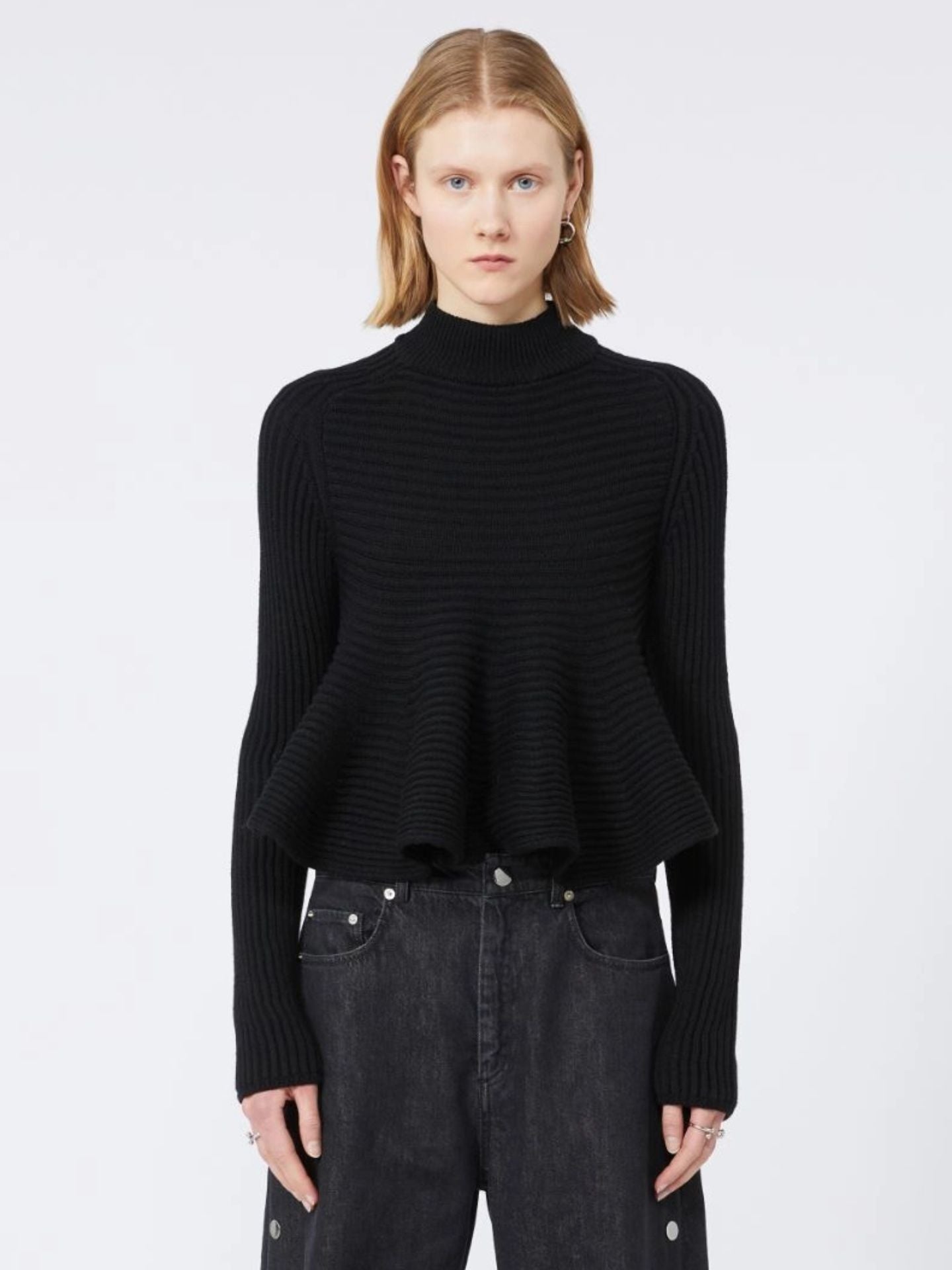 Person wearing a black ribbed sweater and dark jeans on a white background