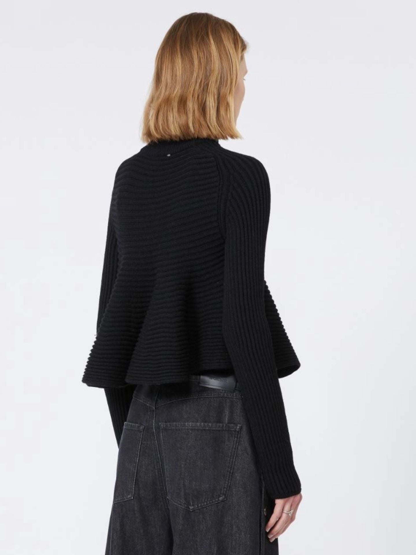 Person wearing a black ribbed sweater and dark pants on a white background