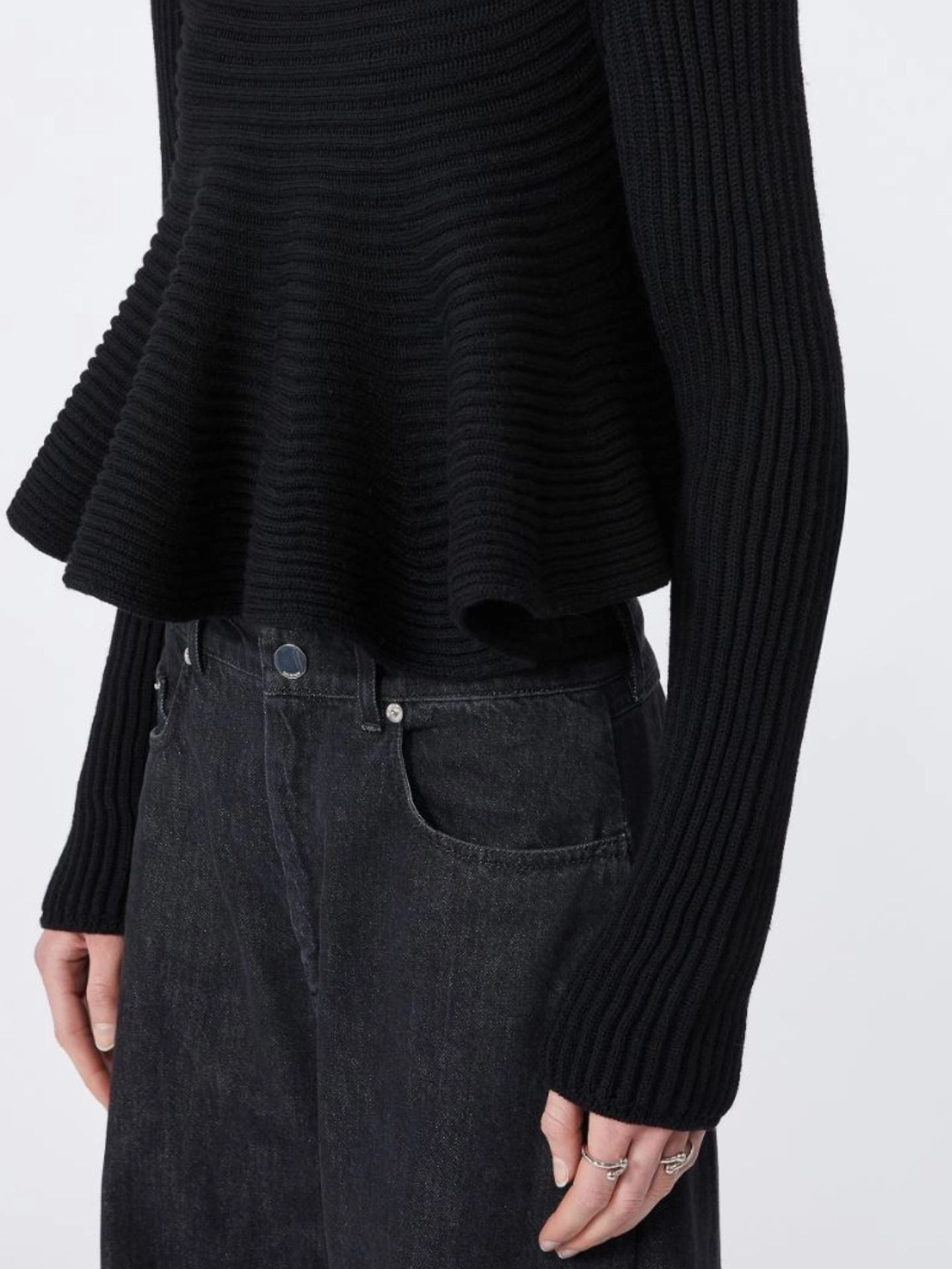 Person wearing a black ribbed sweater and dark jeans on a white background