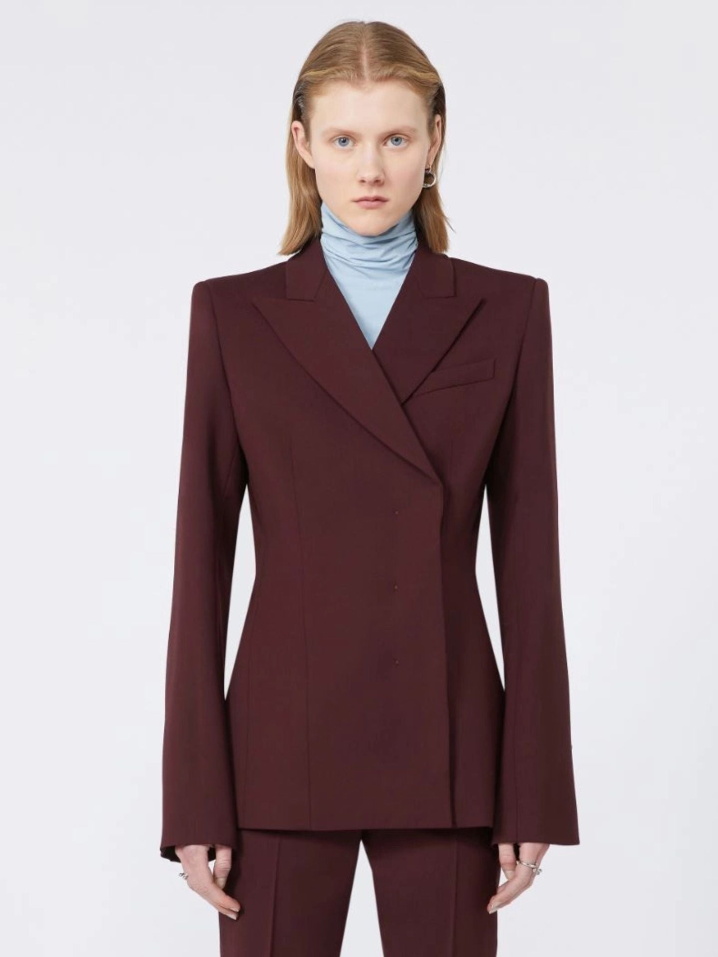 Woman wearing a burgundy suit with a light blue turtleneck on a white background