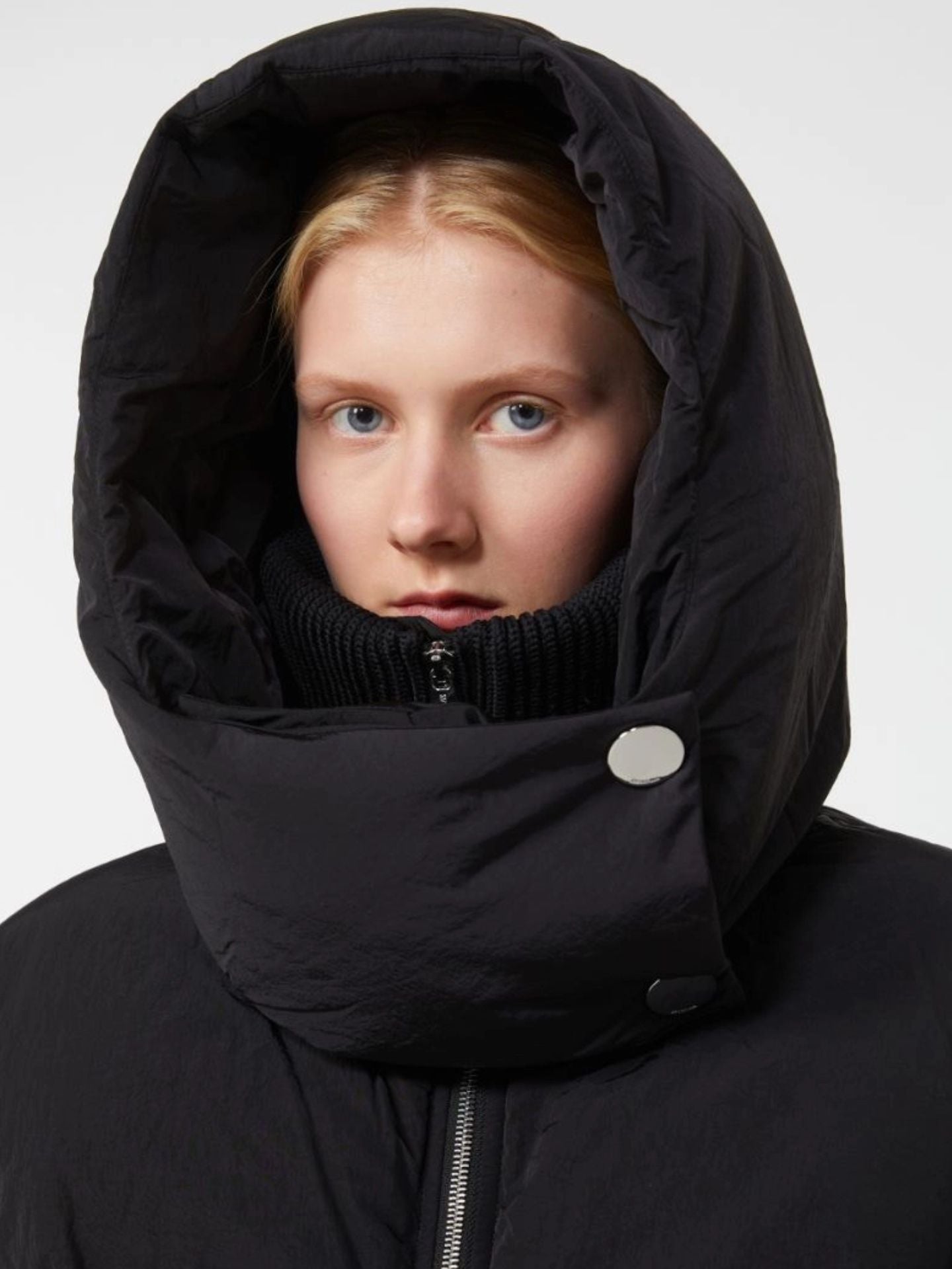 Person wearing a black hooded coat against a white background