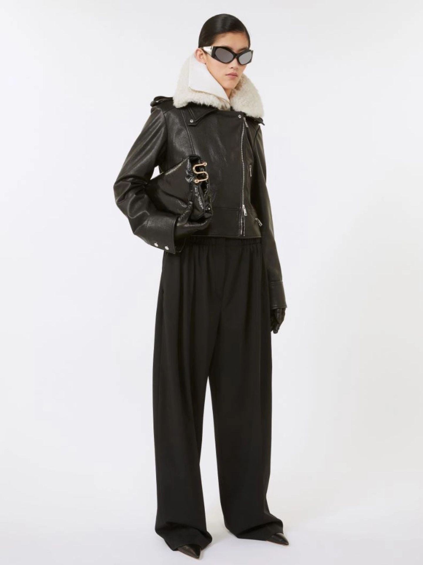 Person wearing a black leather jacket with white fur lining and black pants on a white background