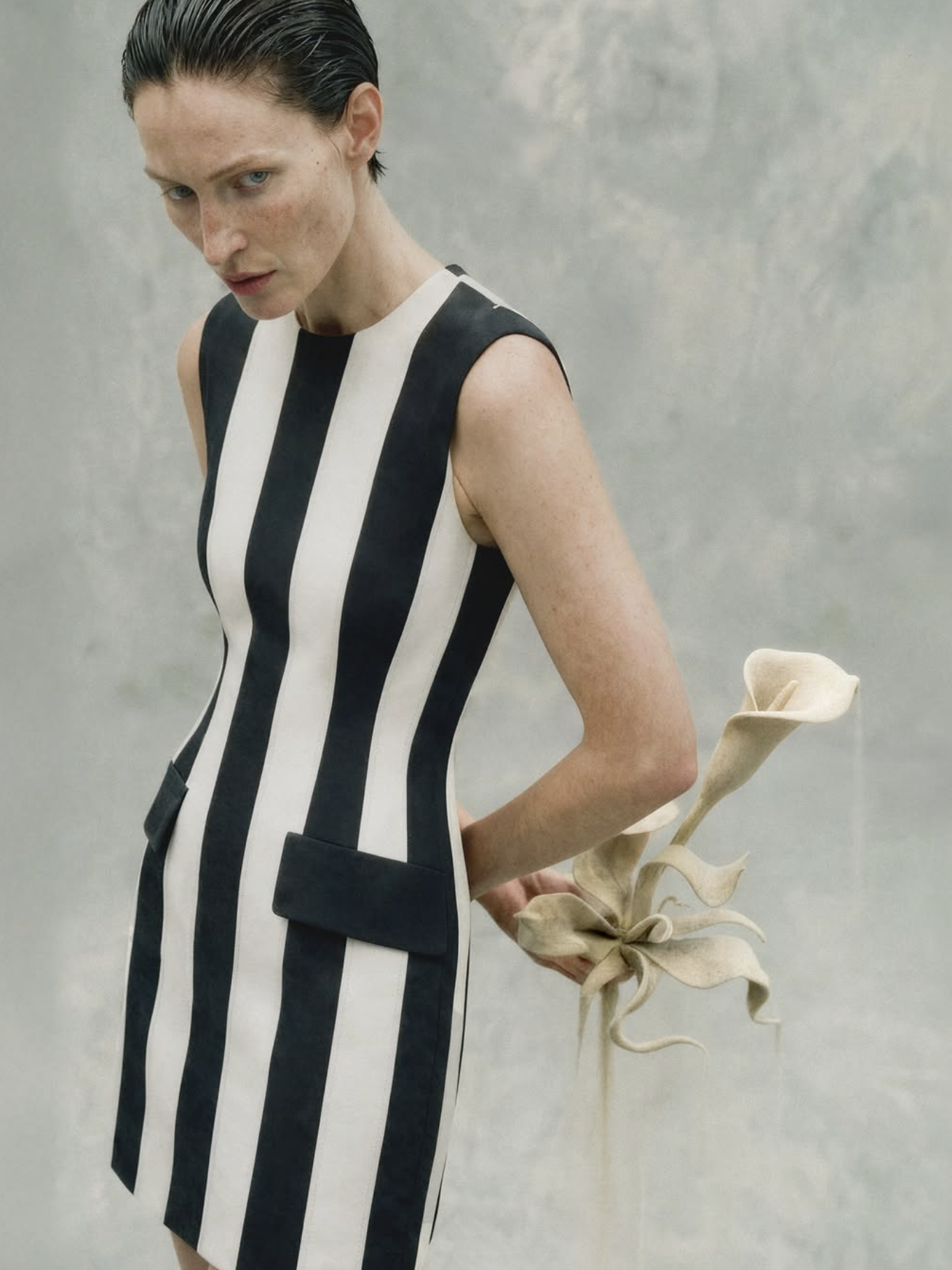 Woman wearing a black and white striped dress holding a dried flower against a gray background