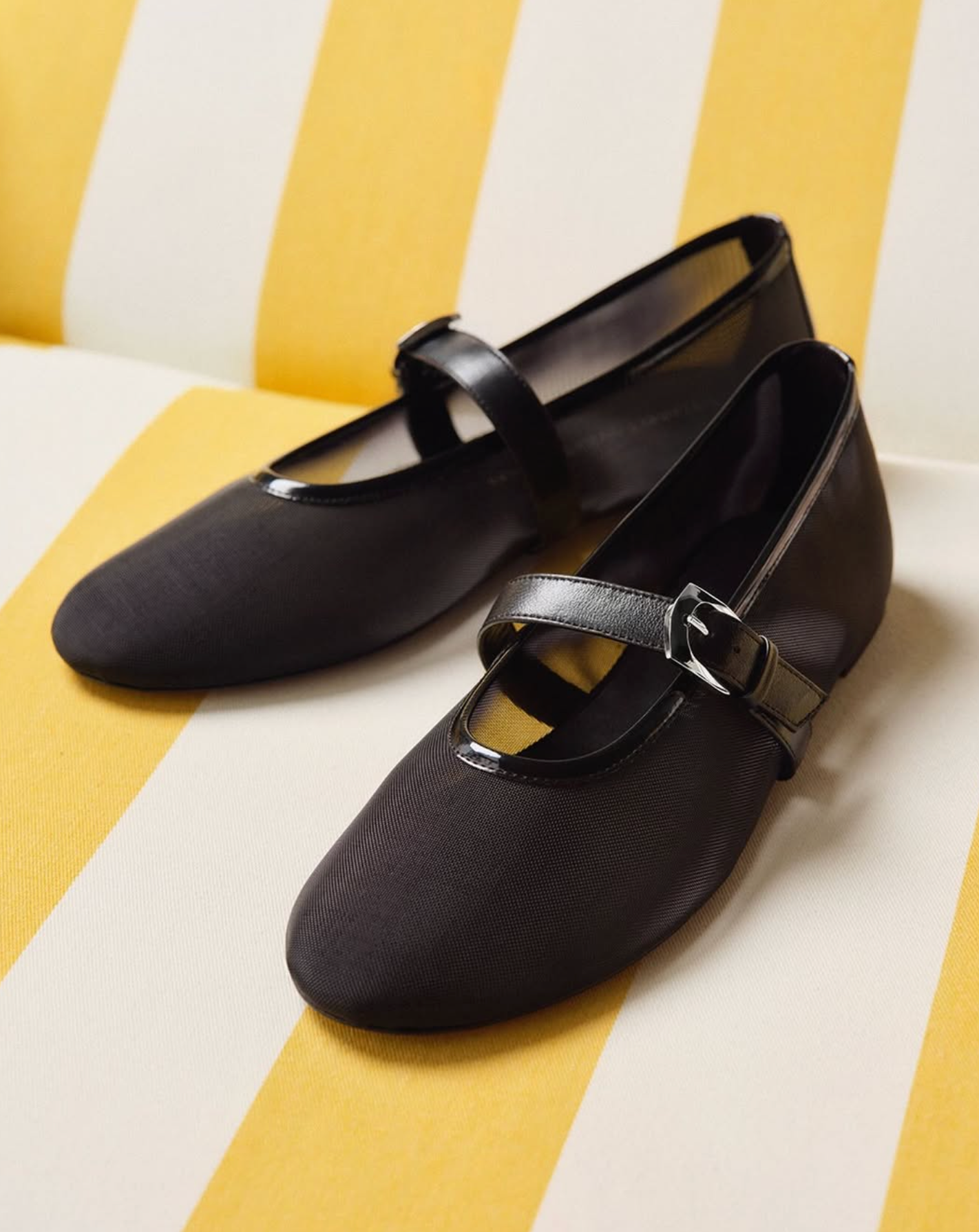Black flat shoes with a strap on a yellow and white striped background