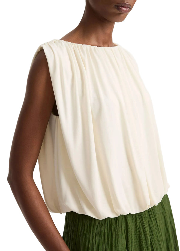 Woman wearing a white sleeveless top and green pleated skirt on a plain background