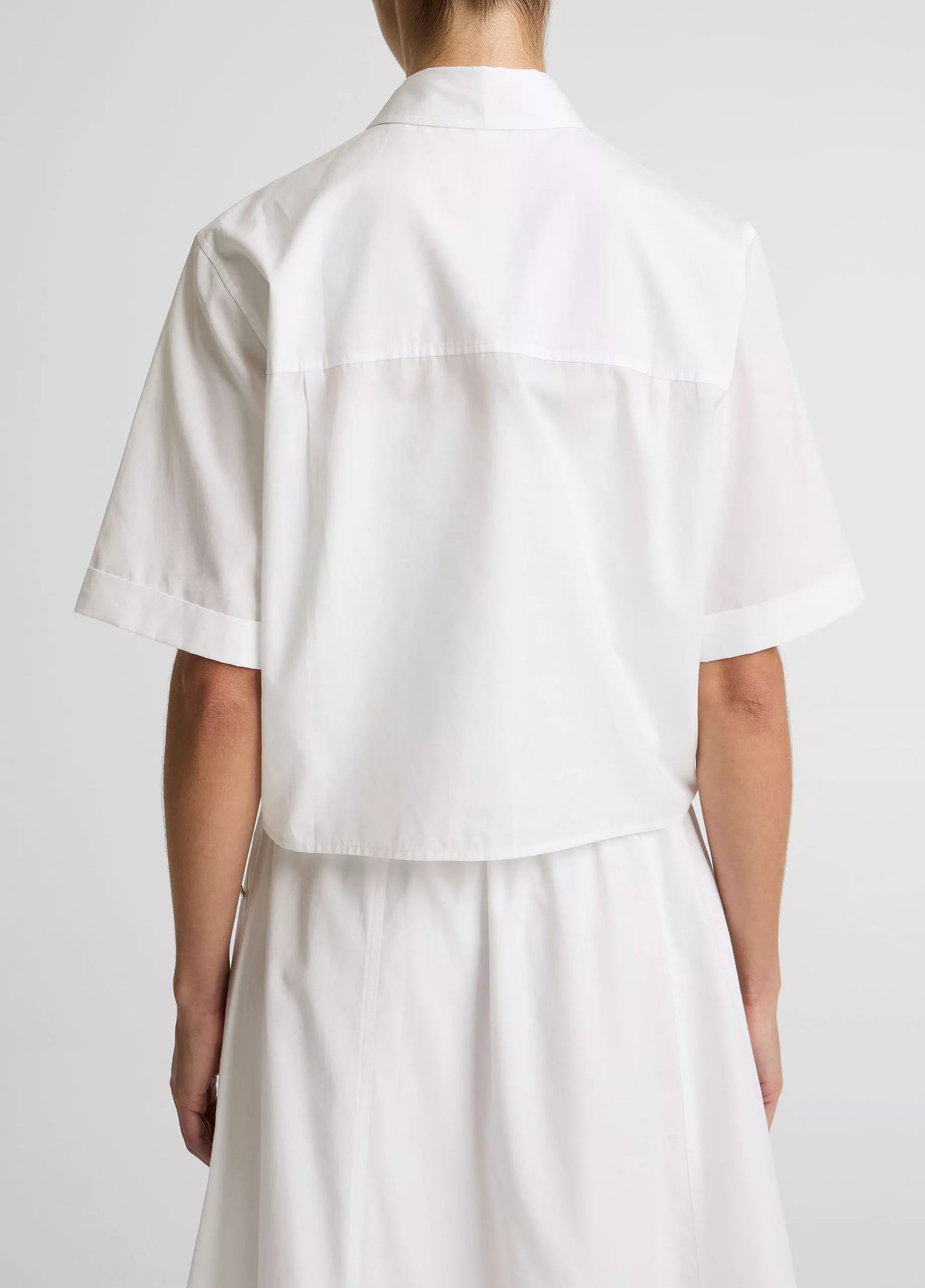 Person wearing a white shirt and skirt set on a plain background