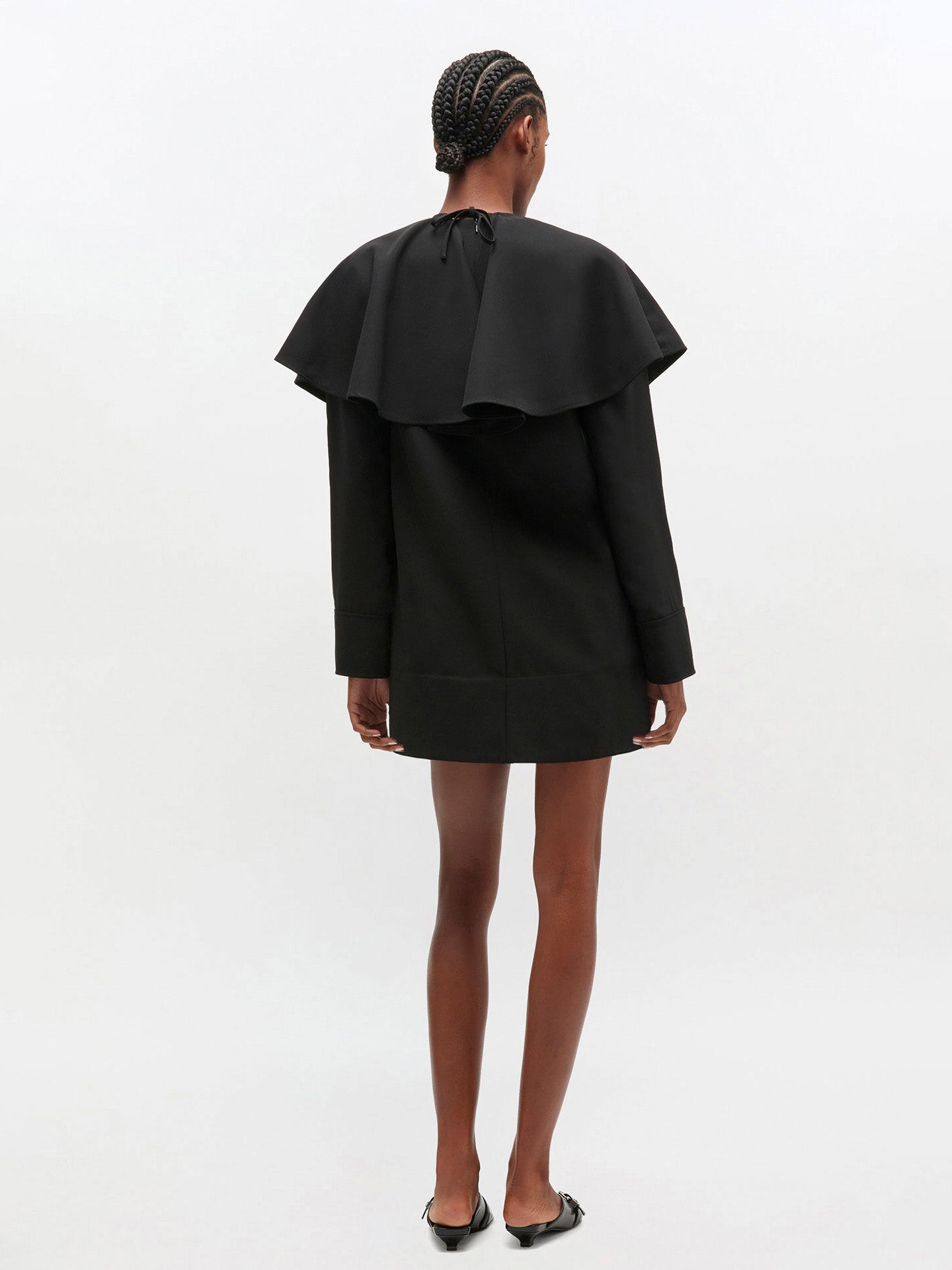 Person wearing a black dress with ruffled shoulders on a white background